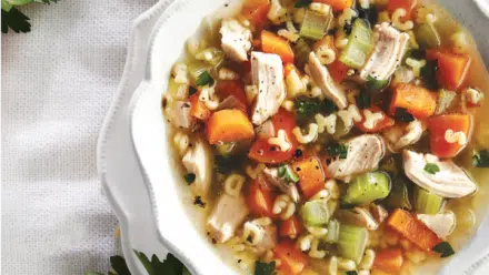 bowl of chicken soup with vegetables and alphabet pasta spelling yummy