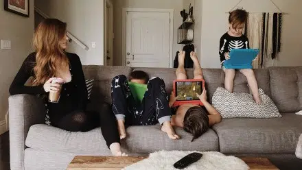 3 kids with iPads on the couch next to their mom enojoying screentime