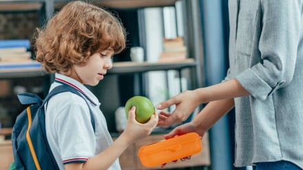 A child holding an apple for school lunch.