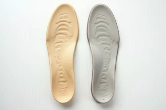 Semelles orthopédiques usées pour pied plat posées sur une surface en bois blanc, montrant des signes évidents d'usure et d'affaissement de l'arche