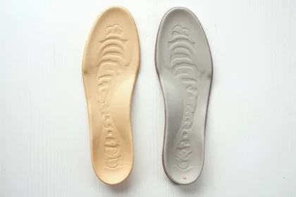 Semelles orthopédiques usées pour pied plat posées sur une surface en bois blanc, montrant des signes évidents d'usure et d'affaissement de l'arche